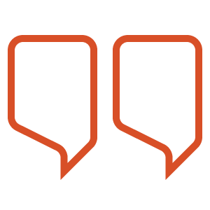An orange, stylized silhouette of a dog is depicted in the image. The dog is shown in a standing pose, facing to the left, with its tail curved slightly upwards. The design is simple and lacks detailed features, emphasizing the shape of the dog.